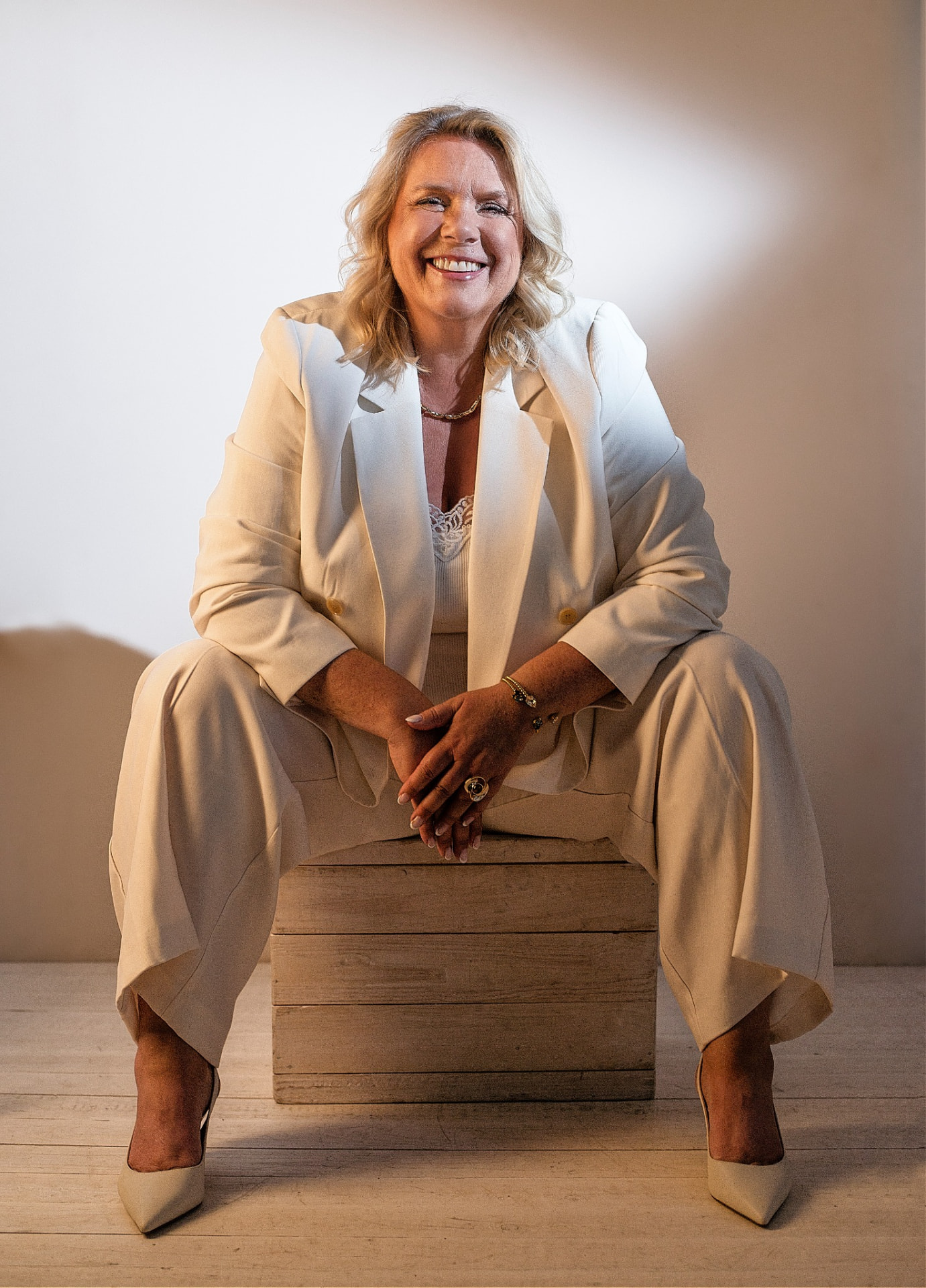 Camilla seated in a cream suit, smiling, in a bright studio
