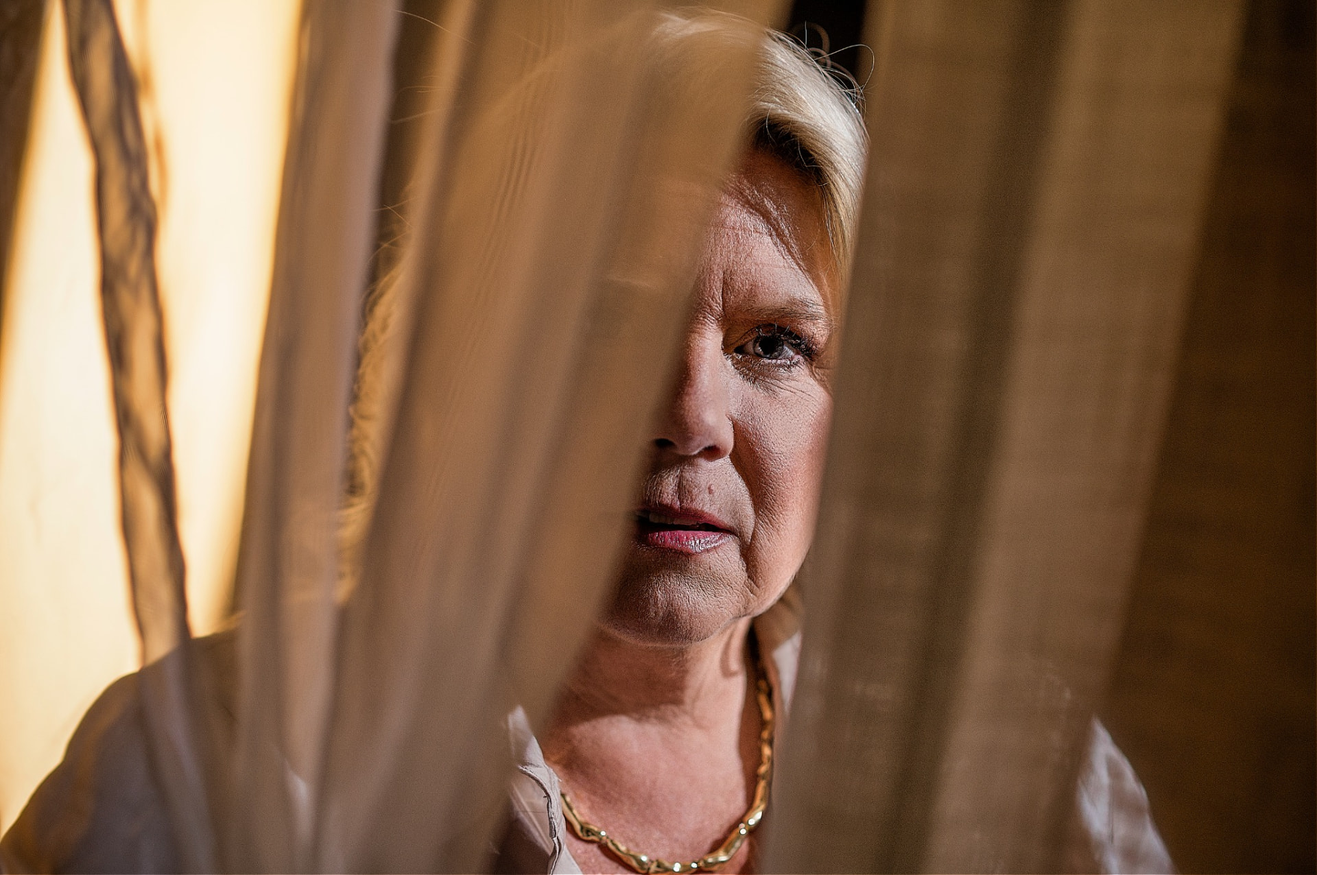 Close portrait of Camilla behind a sheer curtain in warm light