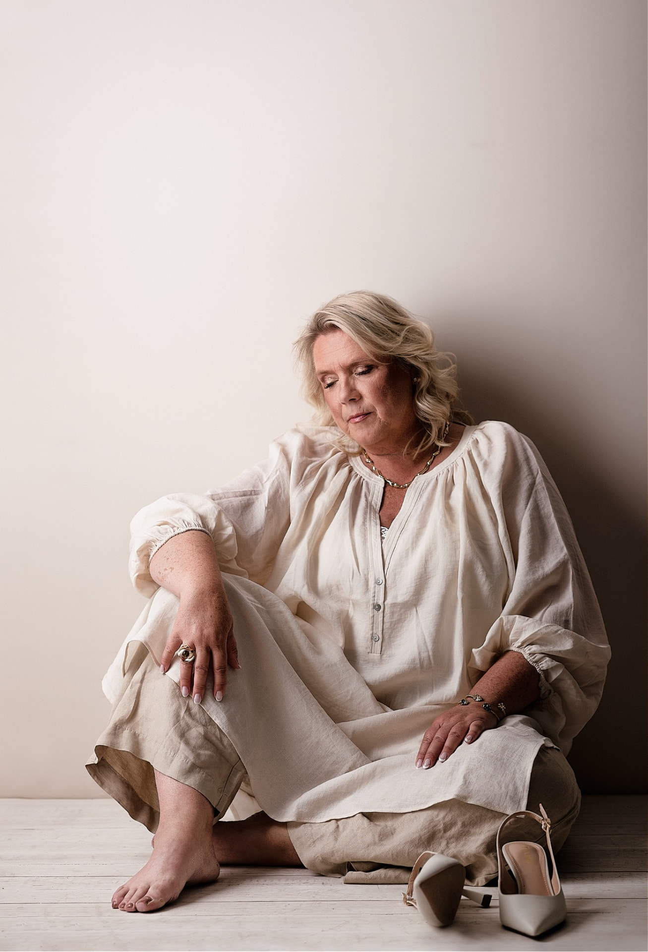 Camilla seated on the floor in cream linen against a bare wall
