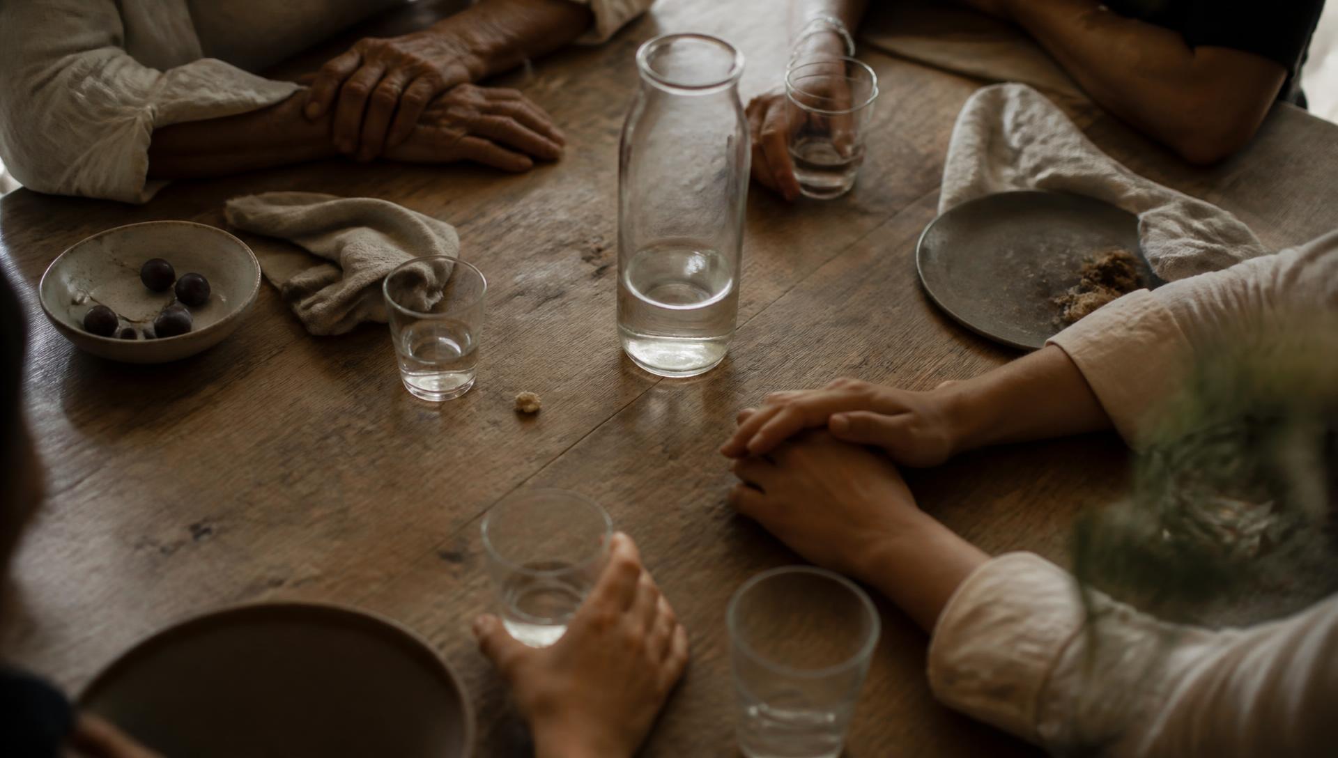 Hands of several generations resting around a worn wooden table