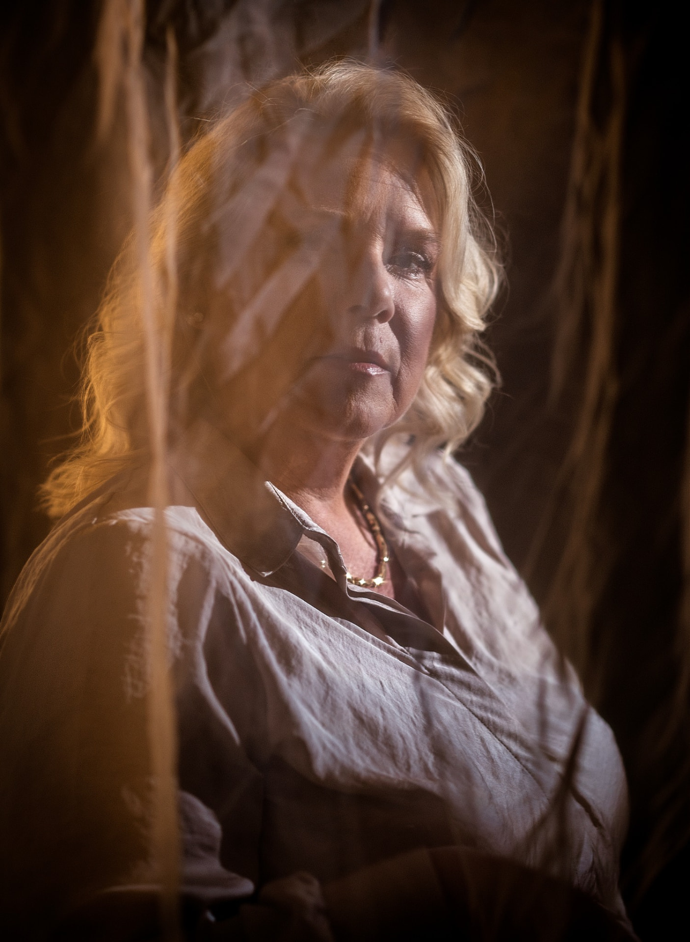 Camilla in warm low light seen through hanging fabric